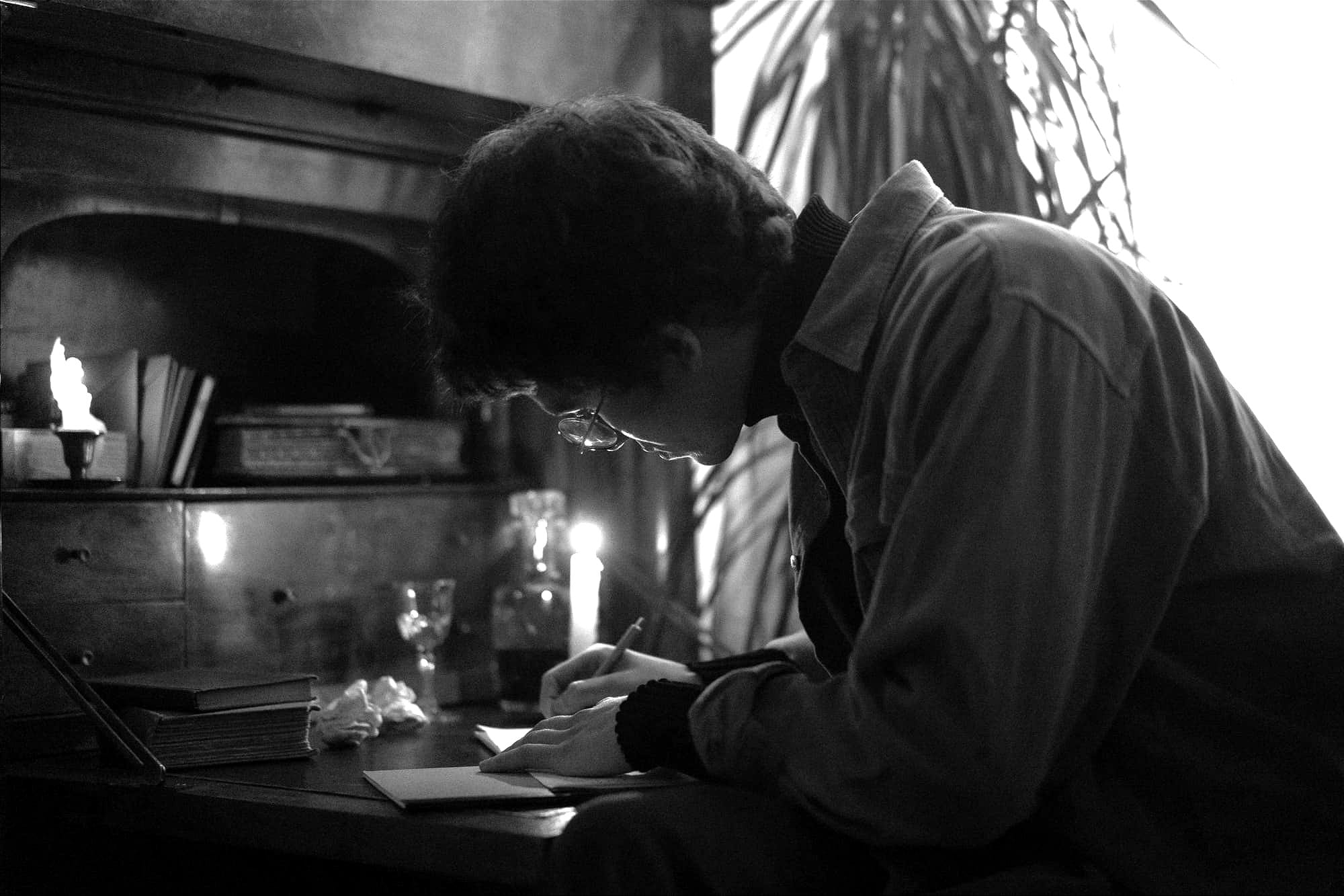 Focused man writing on paper beside a candlelight