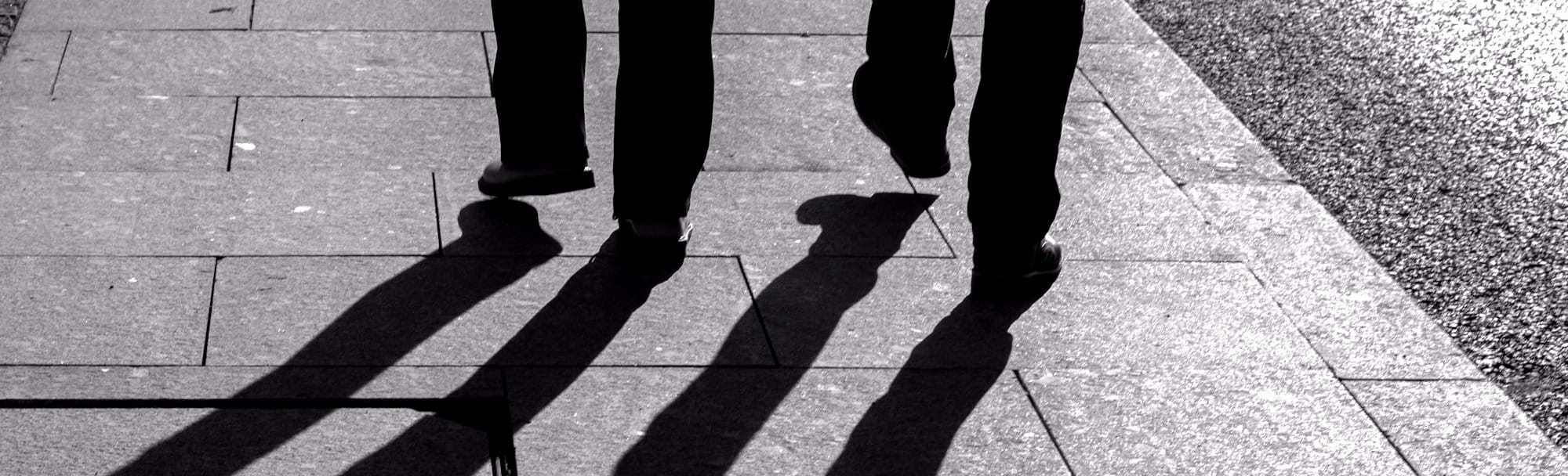Two silhouetted men walking, their shadows stretching away from them.