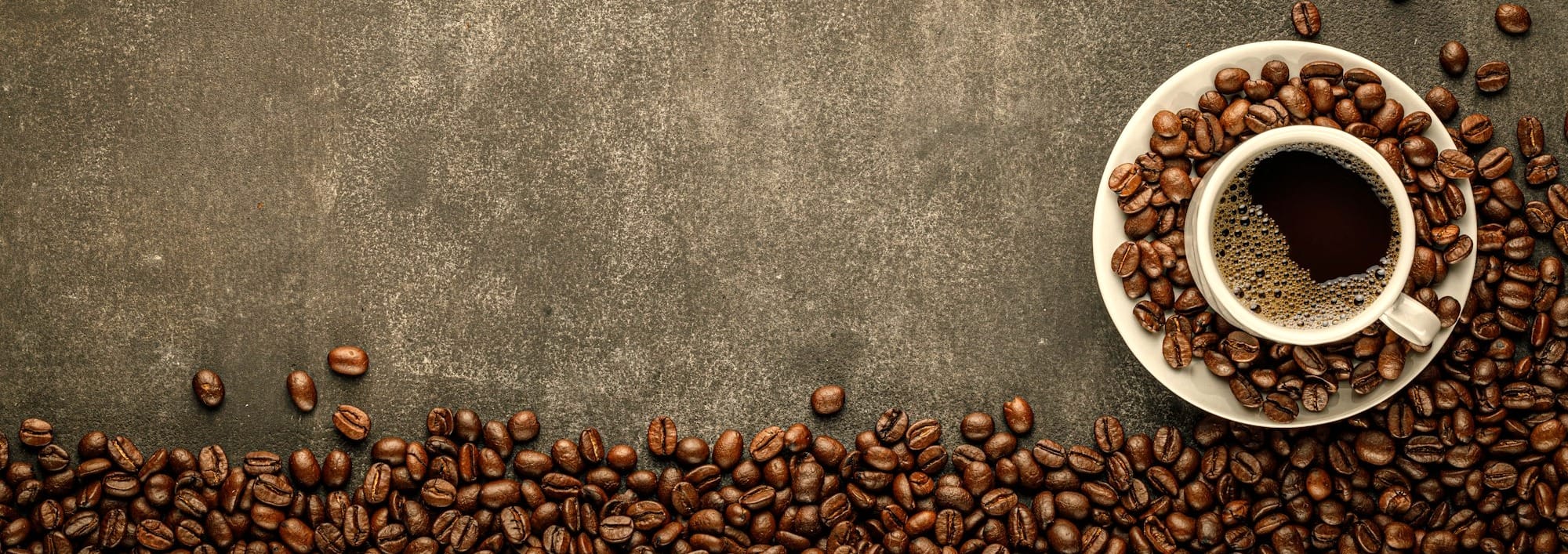 Coffee in cup on saucer sitting on concrete surface surrounded by coffee beans.
