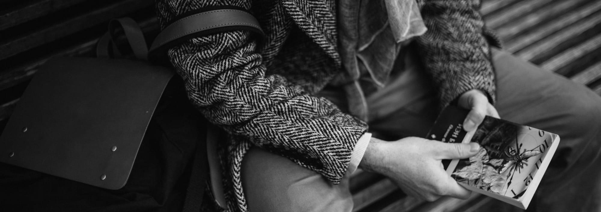Man sitting on bench with bag and book, waiting.