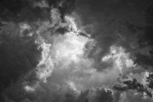 Gray clouds parting in the center to reveal a glowing white cumulus cloud.