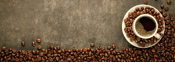 Coffee in cup on saucer sitting on concrete surface surrounded by coffee beans.